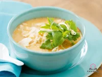 A bowl of coconut chicken and rice soup topped with fresh bean sprouts, mint leaves, and coriander, served in a white bowl with a golden coconut broth