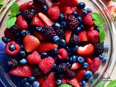 A white bowl filled with fresh strawberries, blueberries, blackberries, and raspberries lightly sprinkled with sugar