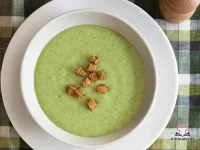 A bowl of creamy cream of broccoli soup garnished with small broccoli florets and a swirl of cream on a rustic wooden table