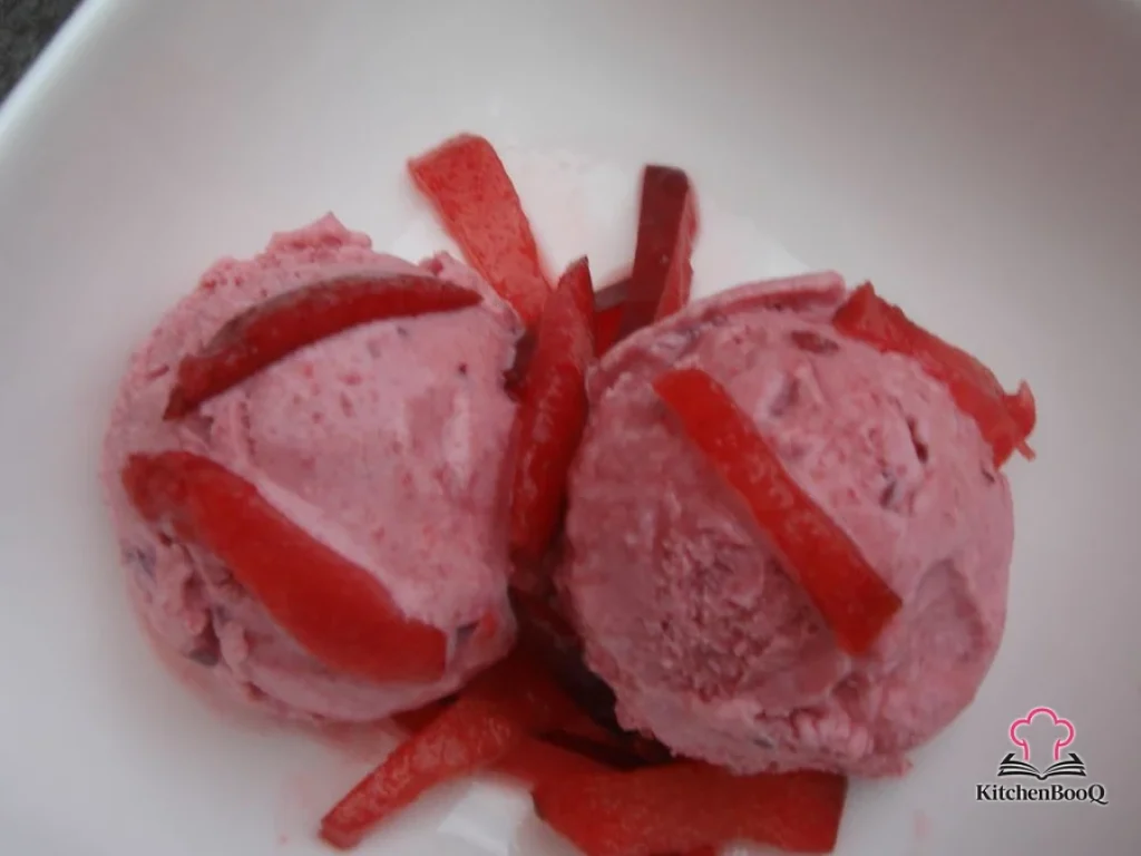Scoops of deep ruby blood plum sherbet in a white bowl topped with fresh sugar-dusted plum slices