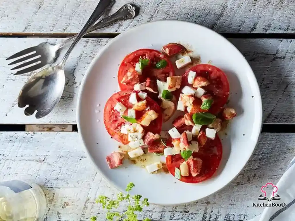 Brown butter lobster caprese salad plated with fanned beefsteak tomato slices, diced fresh mozzarella, tender lobster claw meat glistening in golden brown butter, and torn fresh basil leaves on a white plate