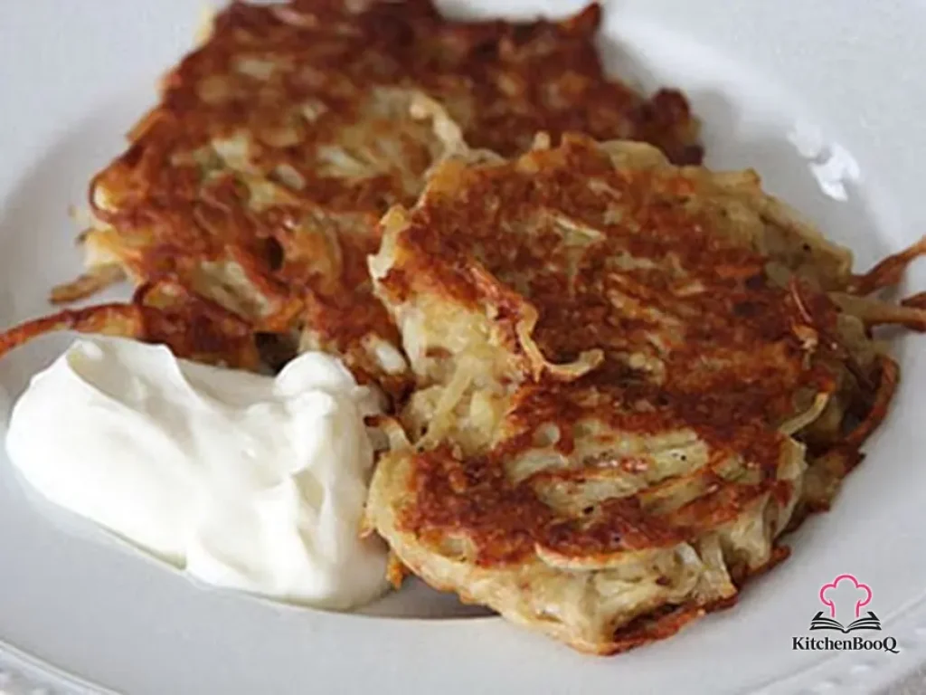 Golden crispy potato latkes stacked on a plate garnished with sour cream and fresh chives on a rustic wooden surface