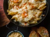 A skillet of cheesy taco penne ziti with golden melted Mexican cheese on top, seasoned ground beef, and tender penne pasta visible beneath the bubbling cheese layer