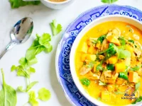 A steaming bowl of chicken and pumpkin soup with shredded chicken, black beans, corn, and fresh cilantro garnish on a rustic wooden table