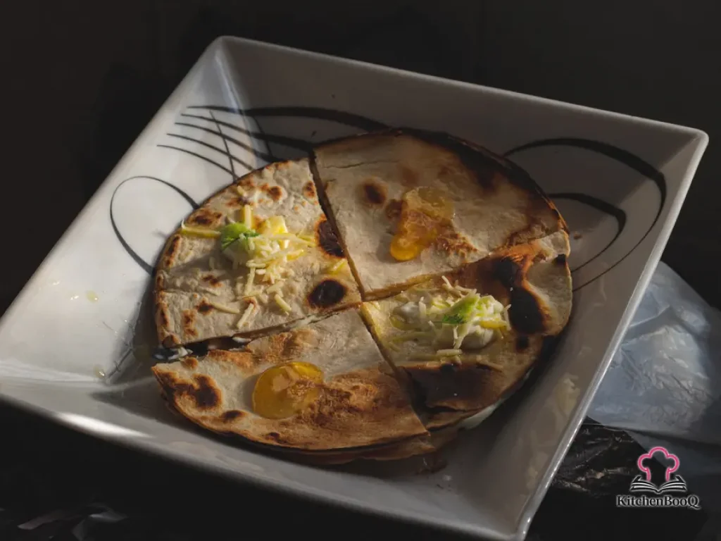 Crispy whole wheat chicken and spinach quesadillas cut into wedges served on a plate with sour cream dipping sauce