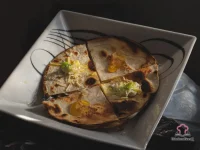 Crispy whole wheat chicken and spinach quesadillas cut into wedges served on a plate with sour cream dipping sauce