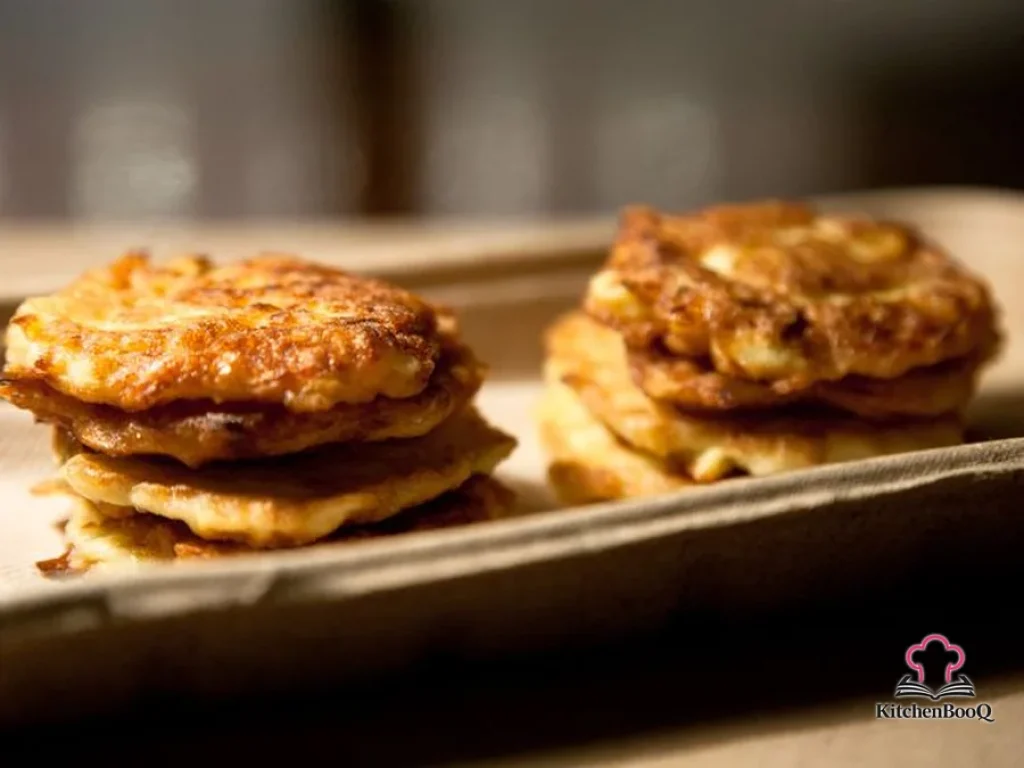 Golden crispy zucchini pancakes stacked on a white plate lined with paper towel, garnished with fresh herbs