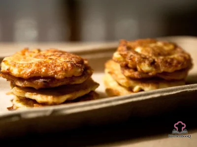 Golden crispy zucchini pancakes stacked on a white plate lined with paper towel, garnished with fresh herbs