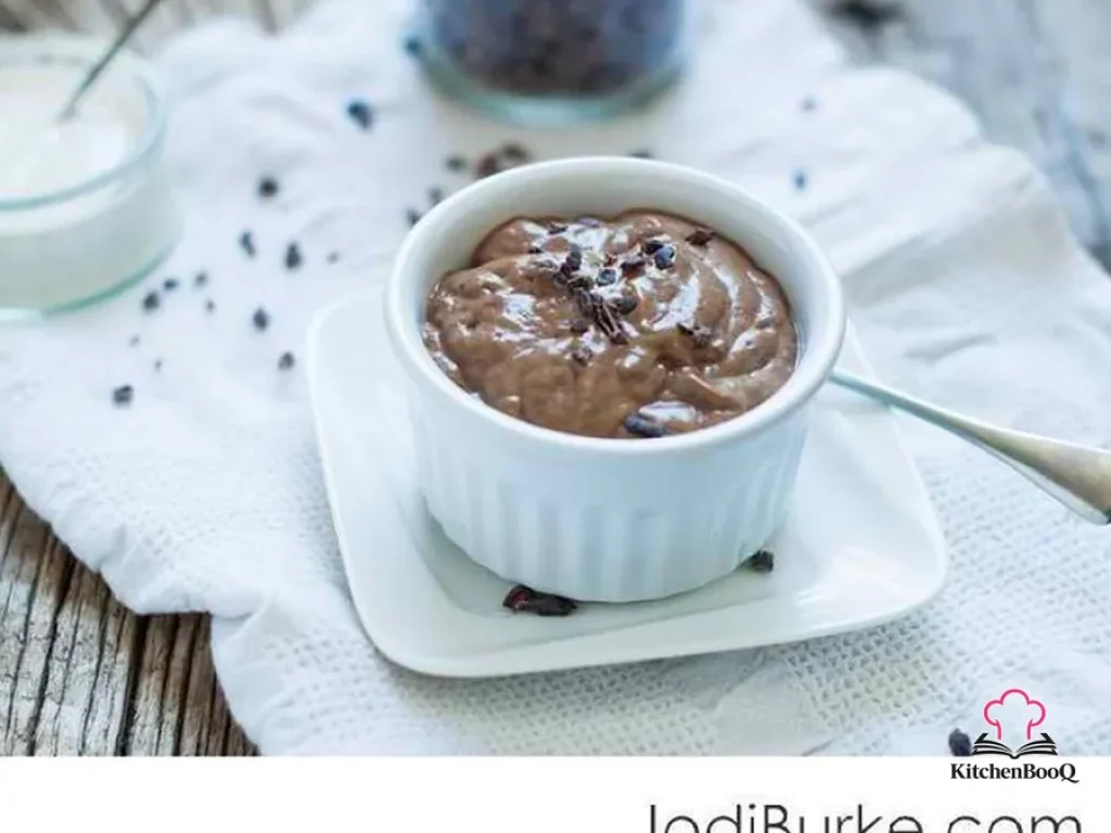 A glass of creamy chocolate chia pudding topped with cacao powder served on a white surface