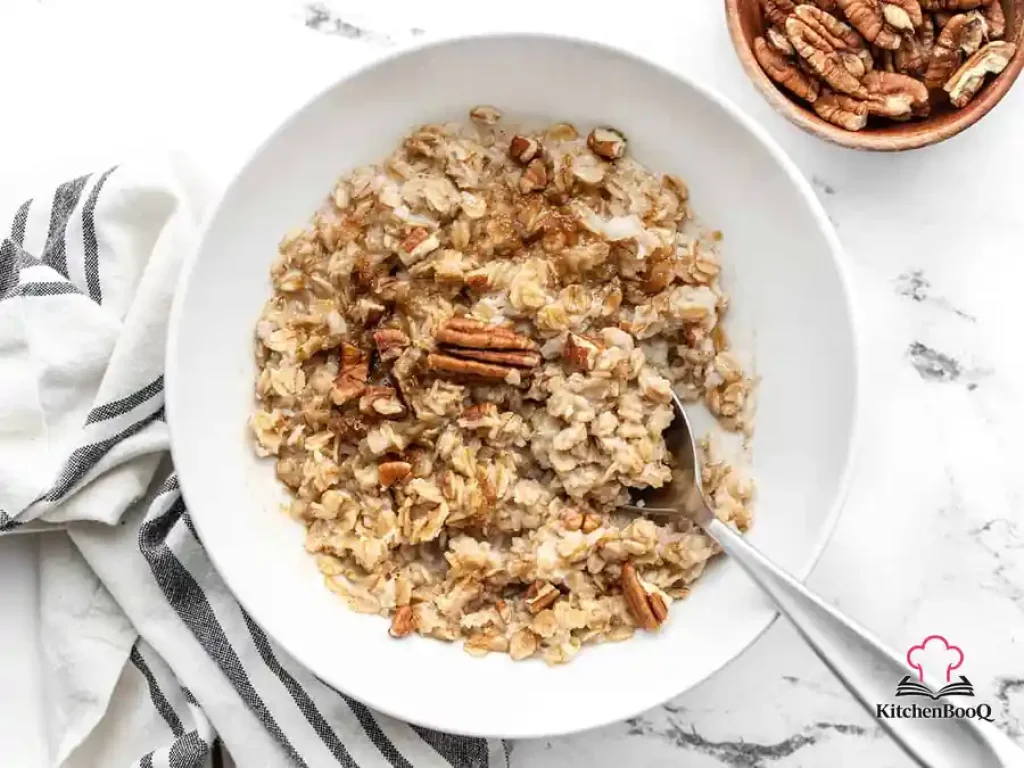 A bowl of creamy cinnamon cauli oats topped with chopped pecans and a sprinkle of brown sugar on a wooden surface