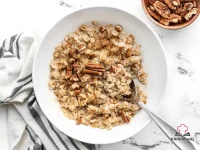 A bowl of creamy cinnamon cauli oats topped with chopped pecans and a sprinkle of brown sugar on a wooden surface