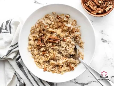 A bowl of creamy cinnamon cauli oats topped with chopped pecans and a sprinkle of brown sugar on a wooden surface