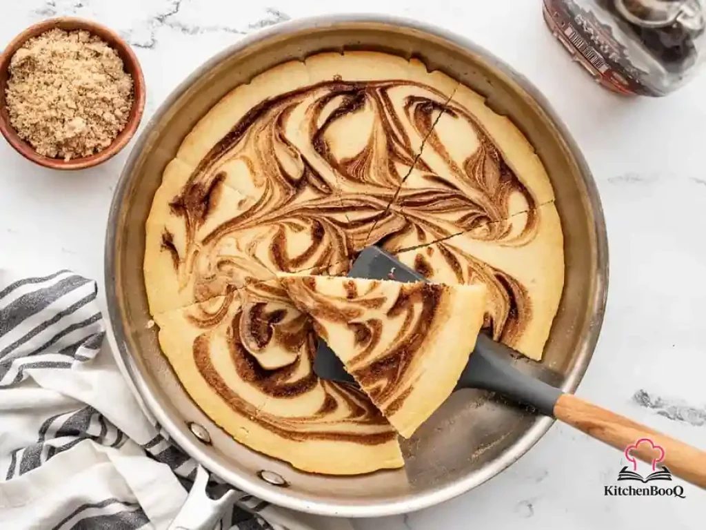 Cinnamon swirl oven pancake sliced into eight wedges in a cast iron skillet, showing a golden top with visible cinnamon swirl pattern