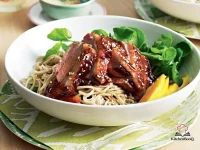 Sliced hoisin-glazed duck breast served over soba noodles with fresh mango slices, watercress sprigs, and sesame-lime dressing on a white plate