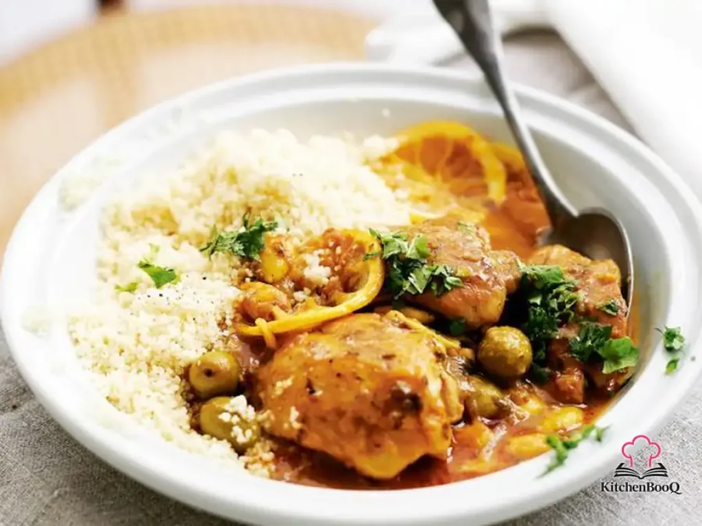 Fast chicken tagine in a large pan with green olives, almonds, lemon slices and fresh coriander served over couscous